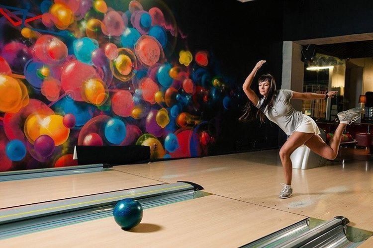Сексуальная блондинка сидит с мячом на полу в боулинг-клубе